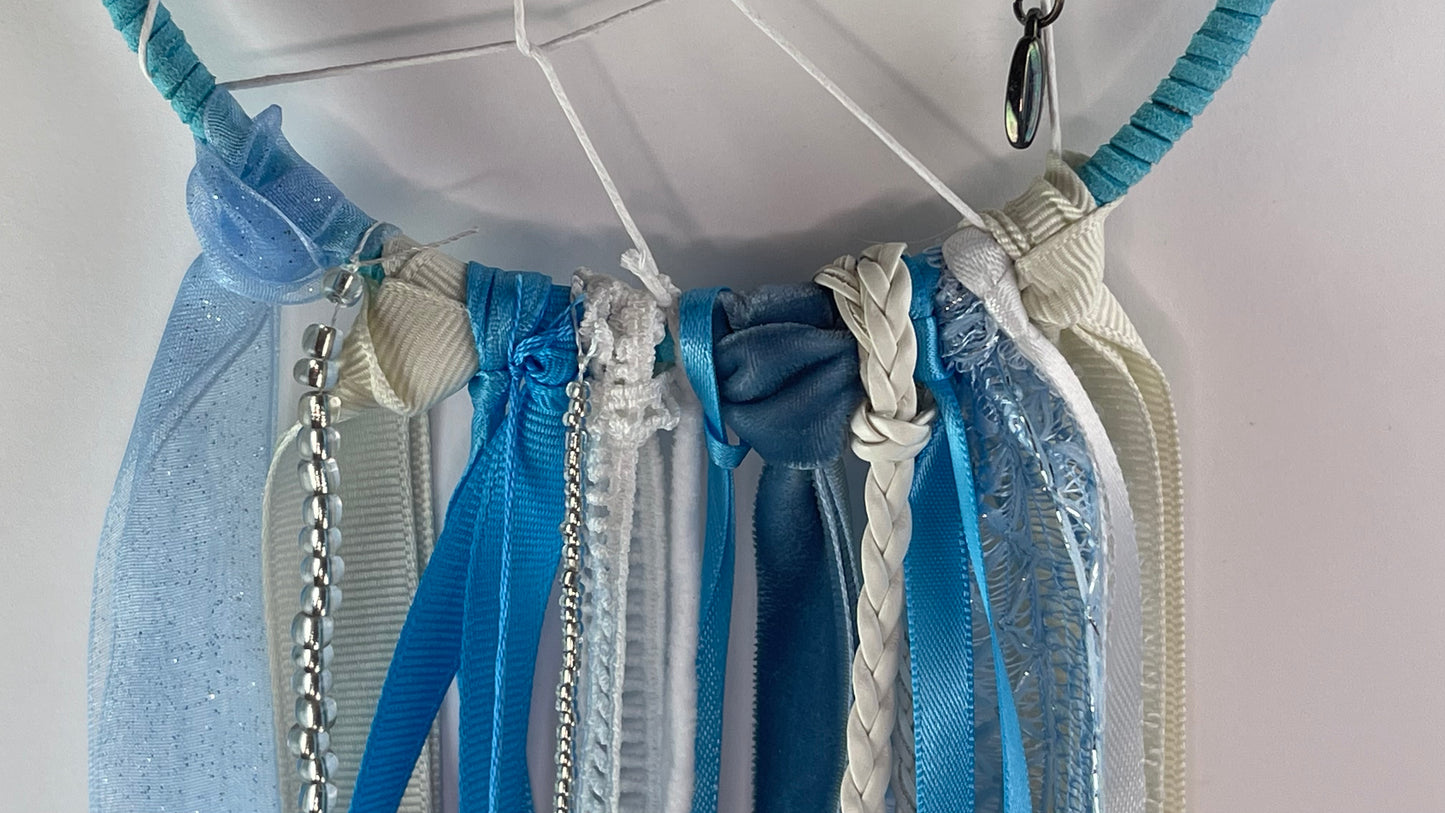 Collection of blue and white ribbons hanging from a dreamcatcher against a white background