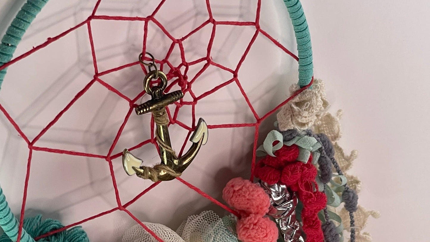 Dreamcatcher with a gold anchor pendant and colorful ribbons on a light pink background